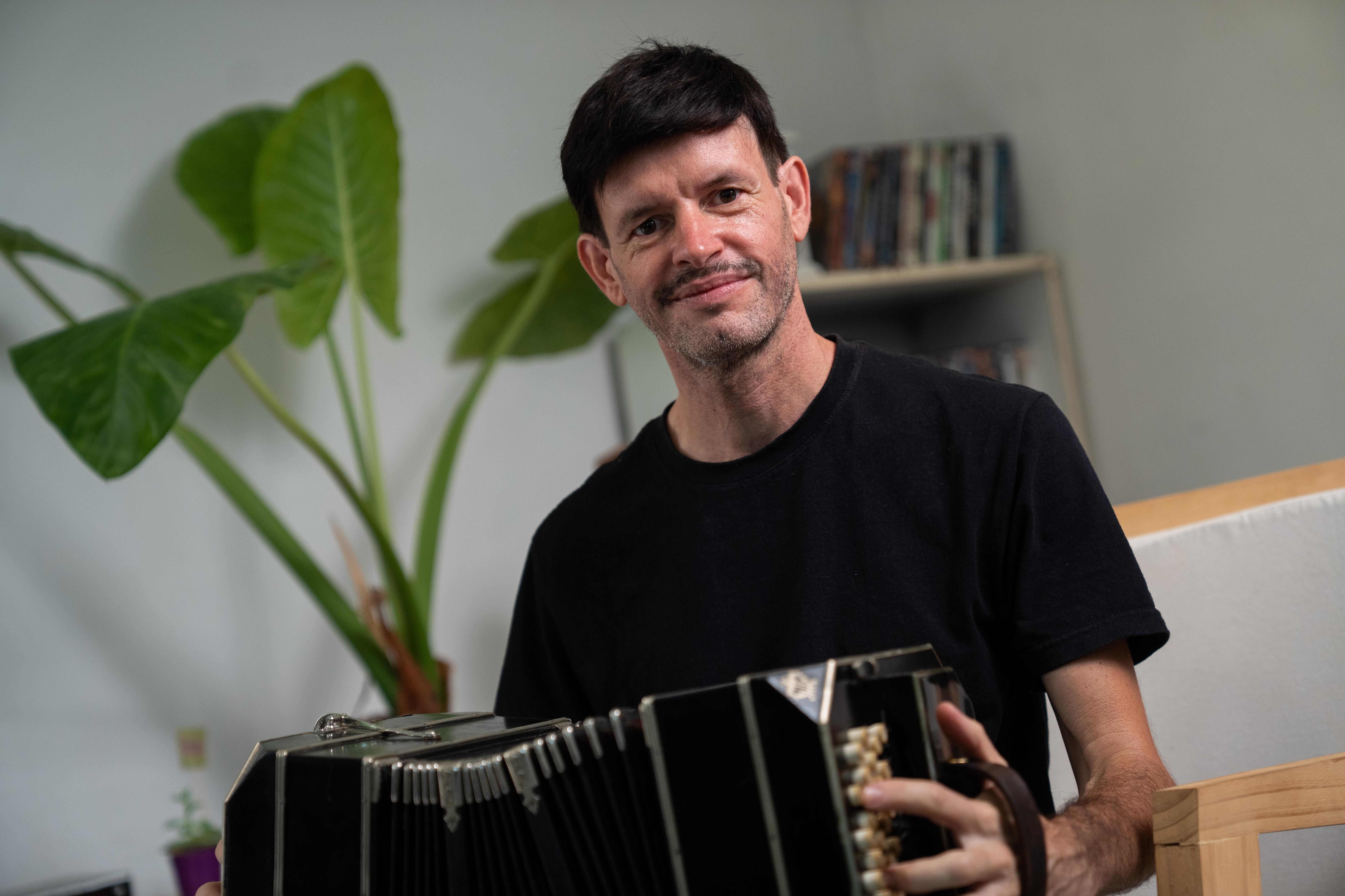 Hombre con playera negra tocando el acordeón en el salón de su casa
