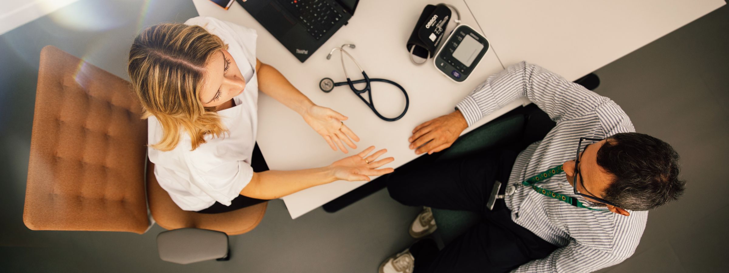 Arzt und Patientin im Gespräch – eine Frau im weißen Hemd erklärt einem Arzt mit Stethoskop etwas an einem modernen Diabetes-Messgerät.