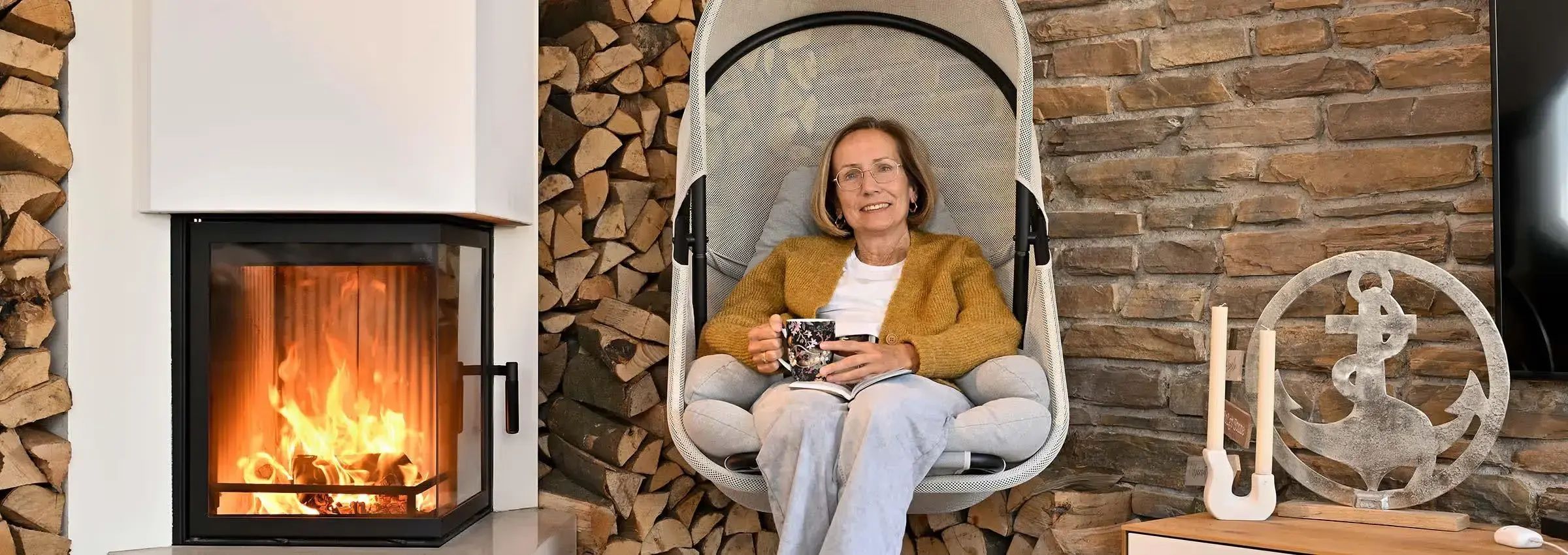 Eva, Patientin mit Multiplem Myelom: In ihrem Wohnzimmer sitzt sie entspannt mit einem Buch und einer Tasse Tee am Kamin – ein Moment der Ruhe, der ihr Kraft im Alltag mit der Erkrankung gibt.