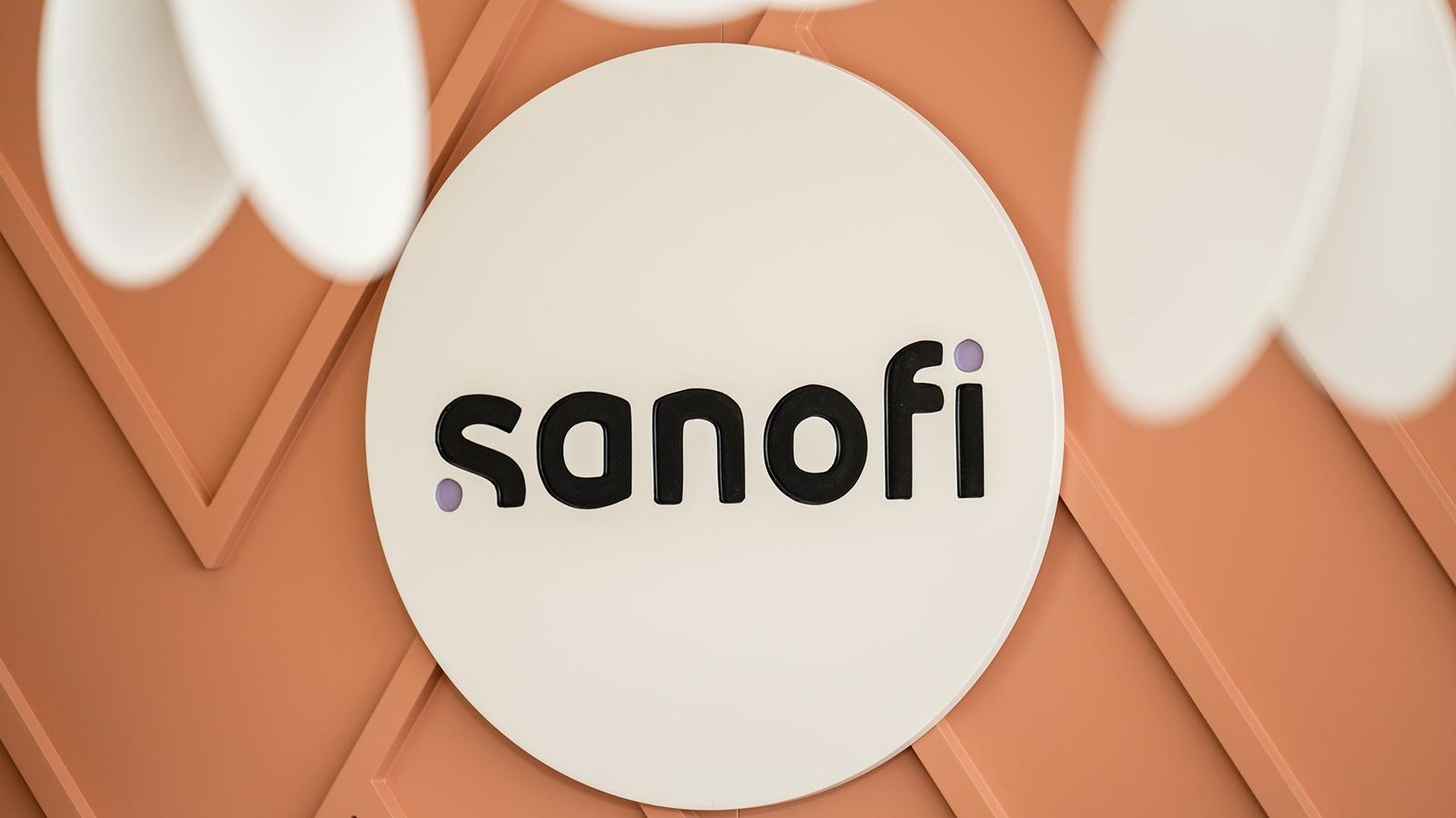 Das Sanofi-Logo in schwarzer Schrift befindet sich in einem weißen Kreis vor einem lebhaften orangen Hintergrund.
