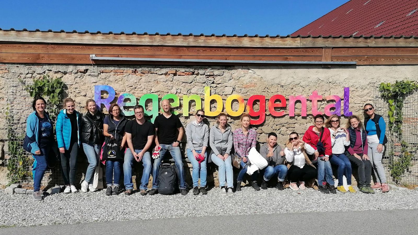 Das Bild zeigt das Sanofi Österreich Team vor dem farbenfrohen Logo des Regenbogentals, einem Therapiehof in Niederösterreich.