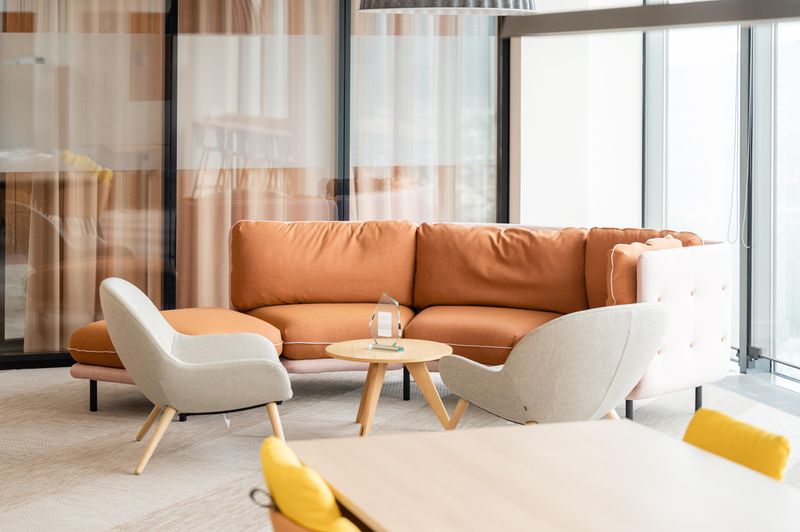 Moderne Lounge mit Ecksofa, grauen Sesseln, runden Holztisch und viel natürlichem Licht durch große Fenster.