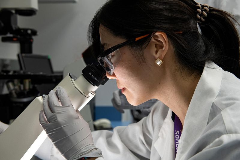 Sung-In Back and Sahar Esmaeili Samani, both wearing white lab coats and safety glasses, examine a partially filled vial