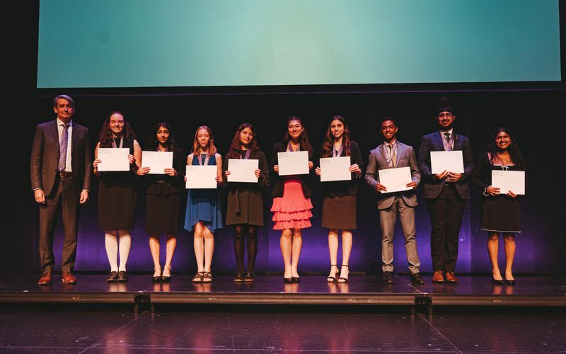 Les neuf lauréats du concours Biogenius 2024, souriant, posent avec leur certificat sur une estrade
