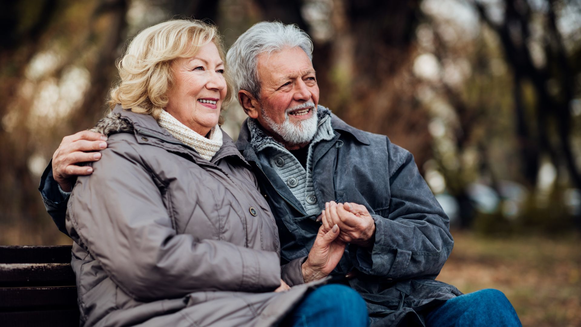 Adultos mayores sentados en un parque, abrazados y sonriendo, con la mirada en algo que acaba de pasar