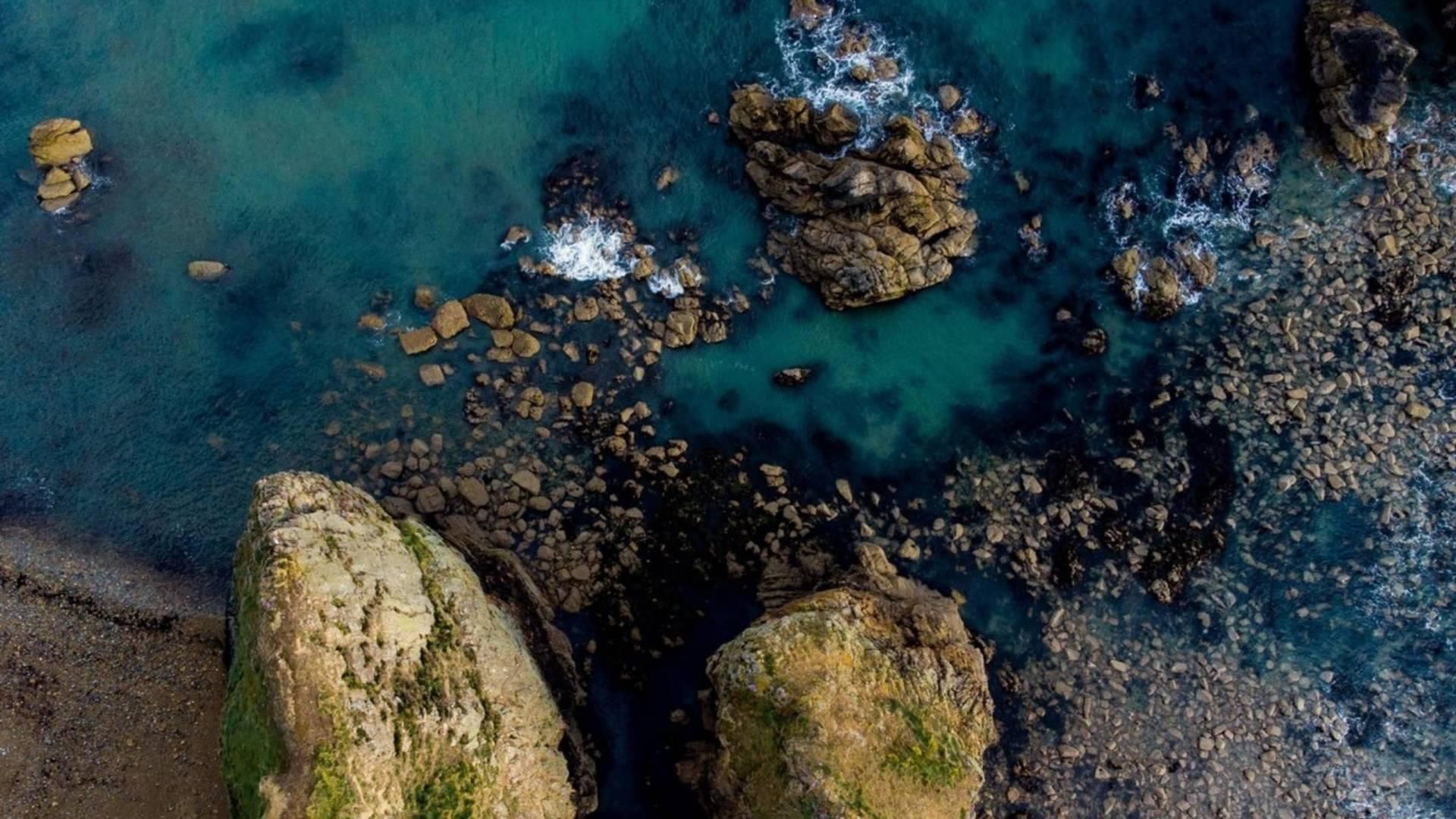 An straight down drone view of Garrarus beach, Waterford Ireland, with sea green waters, coarse sandy beach, and a rocky coast