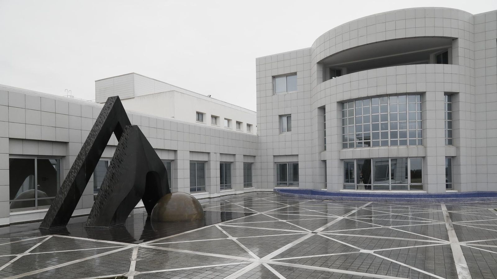 Sanofi Lüleburgaz fabrikasına ait bir beyaz binanın fotoğrafı, bu binanın önünde 3 parçadan oluşan bir heykel bulunmakta. Fotoğraftaki binanın dikdörtgen camları var ve 3. katında bir balkon bulunmakta.