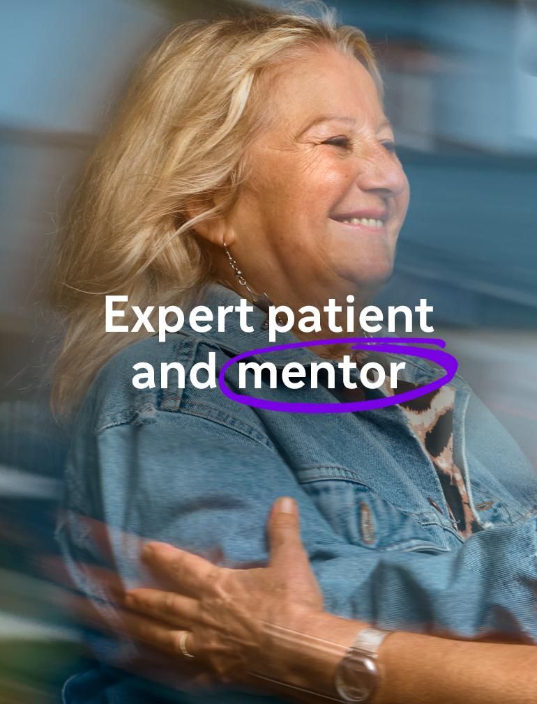 A smiling woman in a blue denim jacket reaches out to embrace another woman wearing glasses. Overlay text reads: "Expert patient and mentor."​