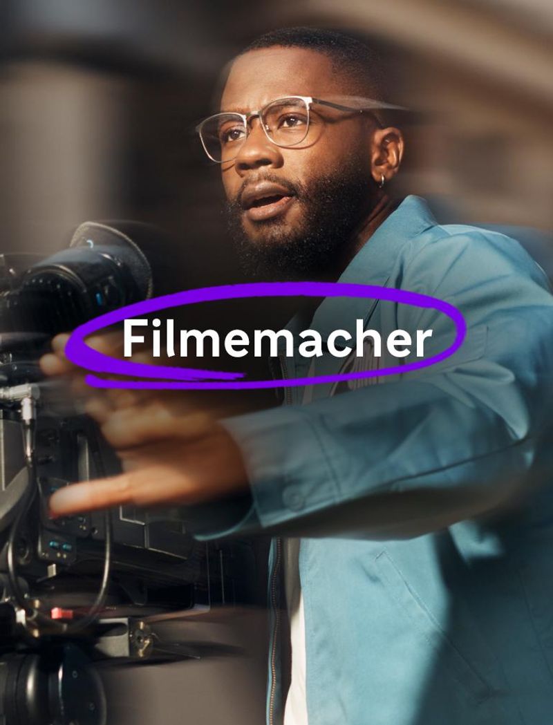Ein Mann mit Brille und blauer Jacke bedient eine Videokamera und wirkt beim Filmen konzentriert, seine Hand ist vor ihm ausgestreckt, während er gestikuliert. Überlagerter Text lautet: „Filmemacher.“