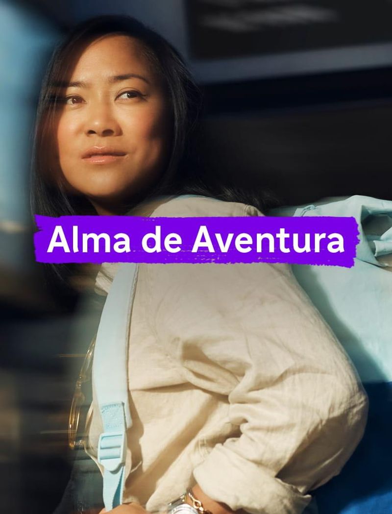 Uma mulher, usando camisa amarela e mochila azul, olha à distância com uma expressão sonhadora. Um texto sobreposto diz: ‘Exploradora.