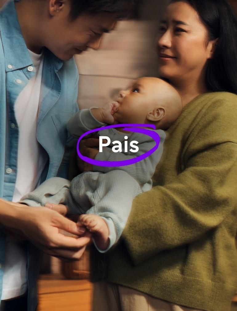 Um homem de camisa azul e uma mulher de suéter verde seguram juntos um bebê pequeno. O bebê está com a mão na boca, olhando para o homem. Um texto sobreposto diz: ‘Pais’.