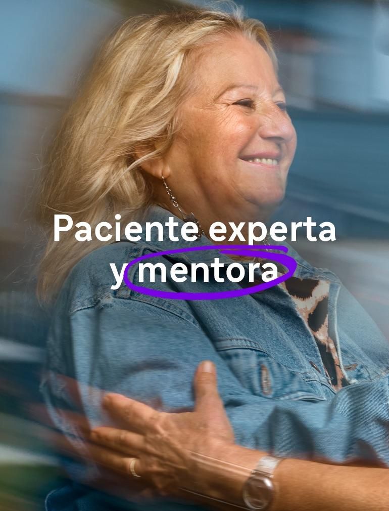 ​ Una mujer sonriente con una chaqueta vaquera extiende la mano para abrazar a otra mujer que también sonríe y lleva gafas.​