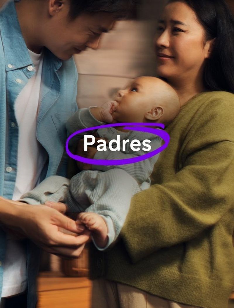  Un hombre con una camisa azul y una mujer con un jersey verde sostienen a un bebé en una habitación cálidamente iluminada. El bebé tiene una mano en la boca y dirige la mirada hacia el hombre.