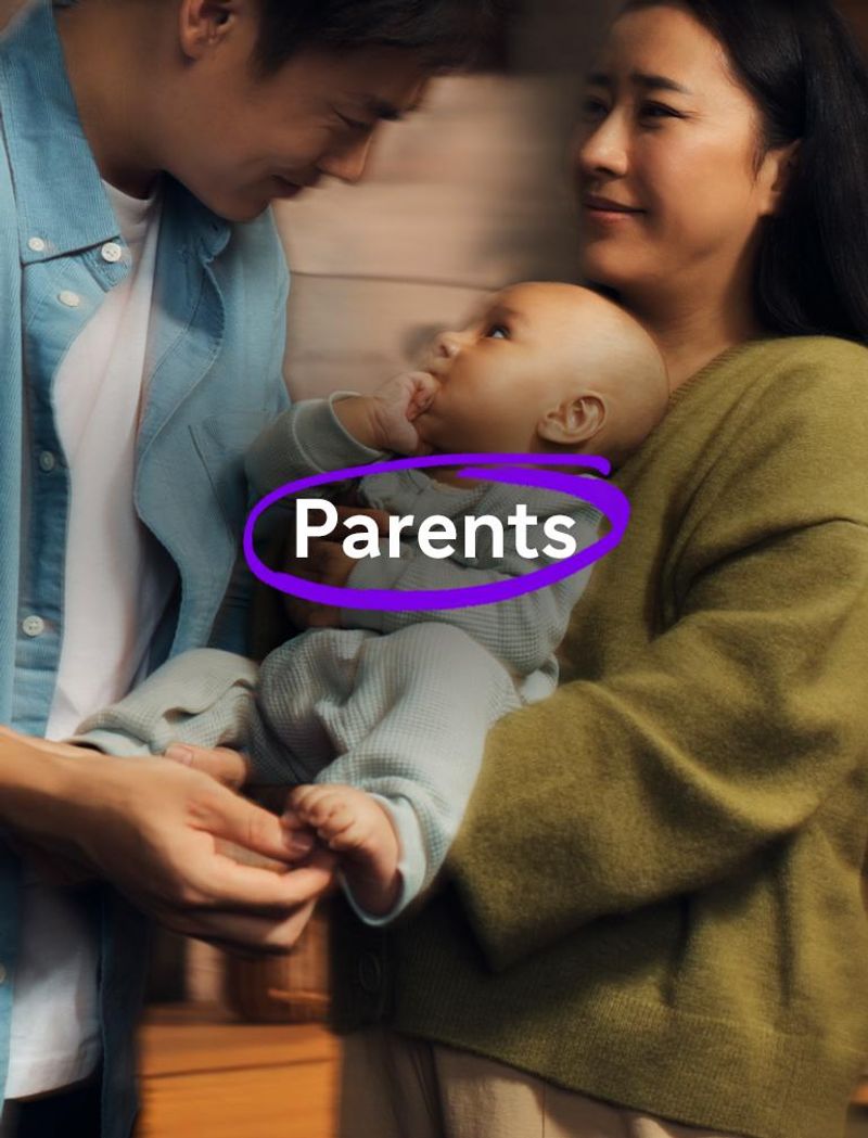 A man in a blue shirt and a woman in a green sweater hold a small baby together. The baby has its hand in its mouth, looking up at the man. Overlay text reads: "Parents."