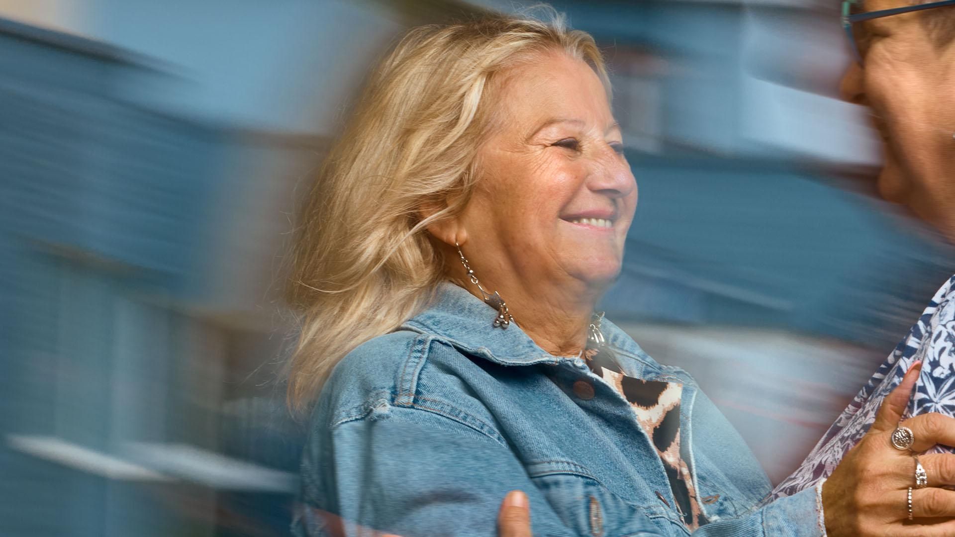Une femme souriante portant une veste en jean tend la main pour étreindre une autre femme souriante portant des lunettes.​