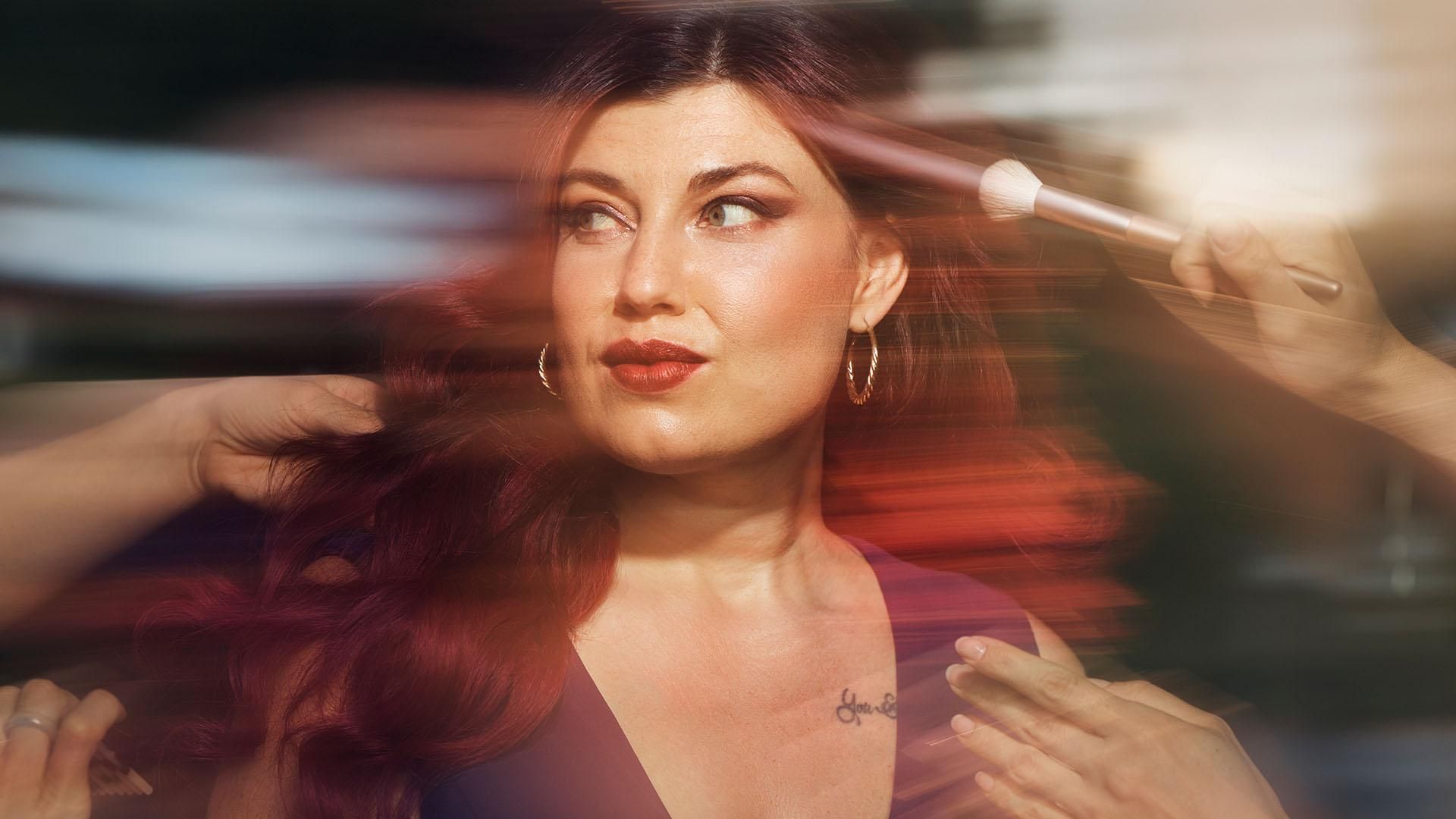 Une femme glamour portant une robe violette est en train de se faire coiffer et maquiller ; elle regarde sur le côté la personne qui lui arrange les cheveux. Le texte en surimpression indique : « Top-model et rôle modèle. »​