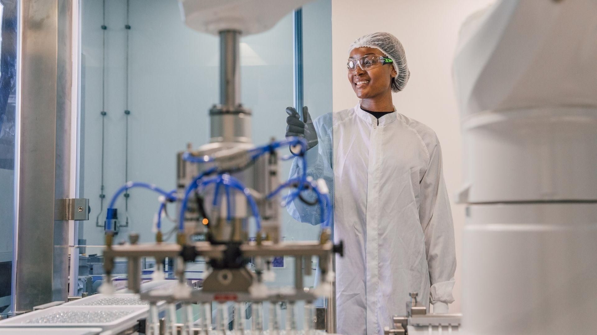 Sanofi employee in protective gear working in a manufacturing laboratory with industrial equipment.