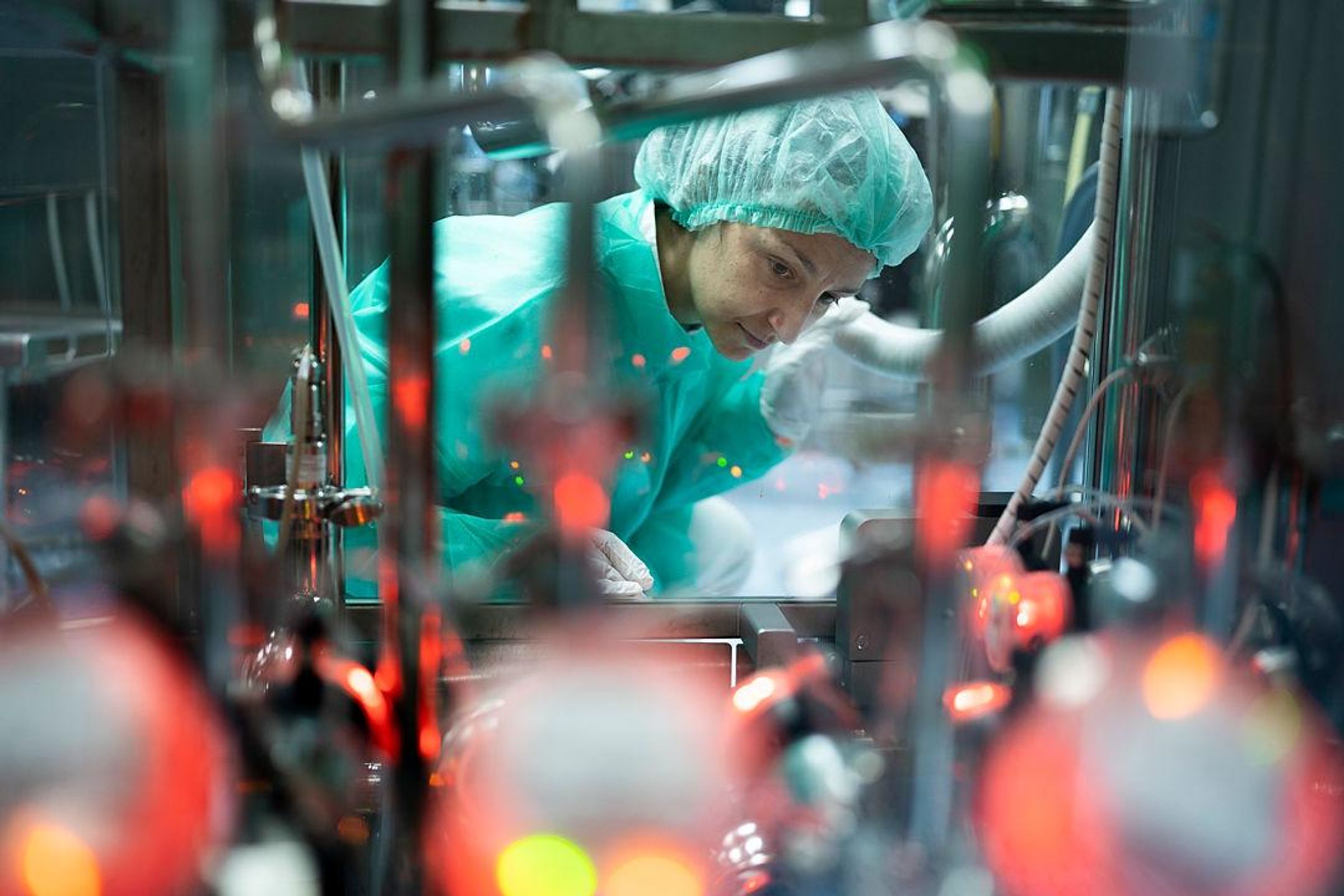 Loredana Ruscito, wearing a light green lab suit and hair net looking at equipment including blurred glowing orange devices