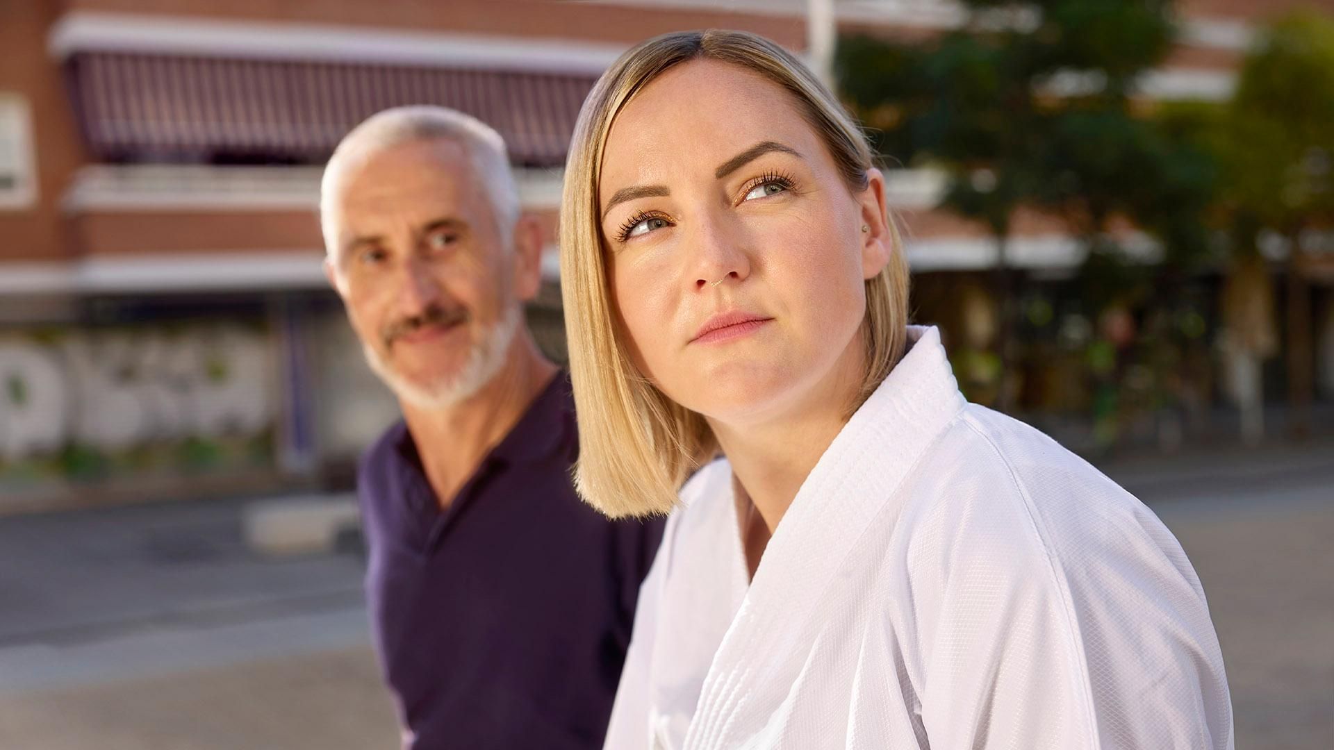 A woman in a white karate outfit is sat with a man in navy t shirt