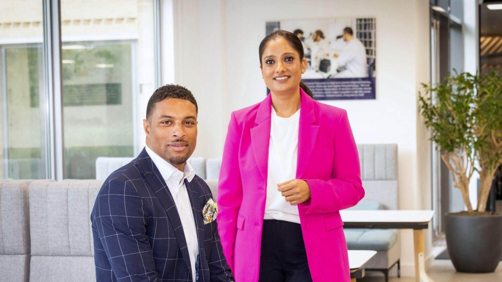 Deux collaborateurs de Sanofi, un homme en costume bleu foncé à carreaux et une femme en blazer rose, échangent dans un environnement de bureau moderne