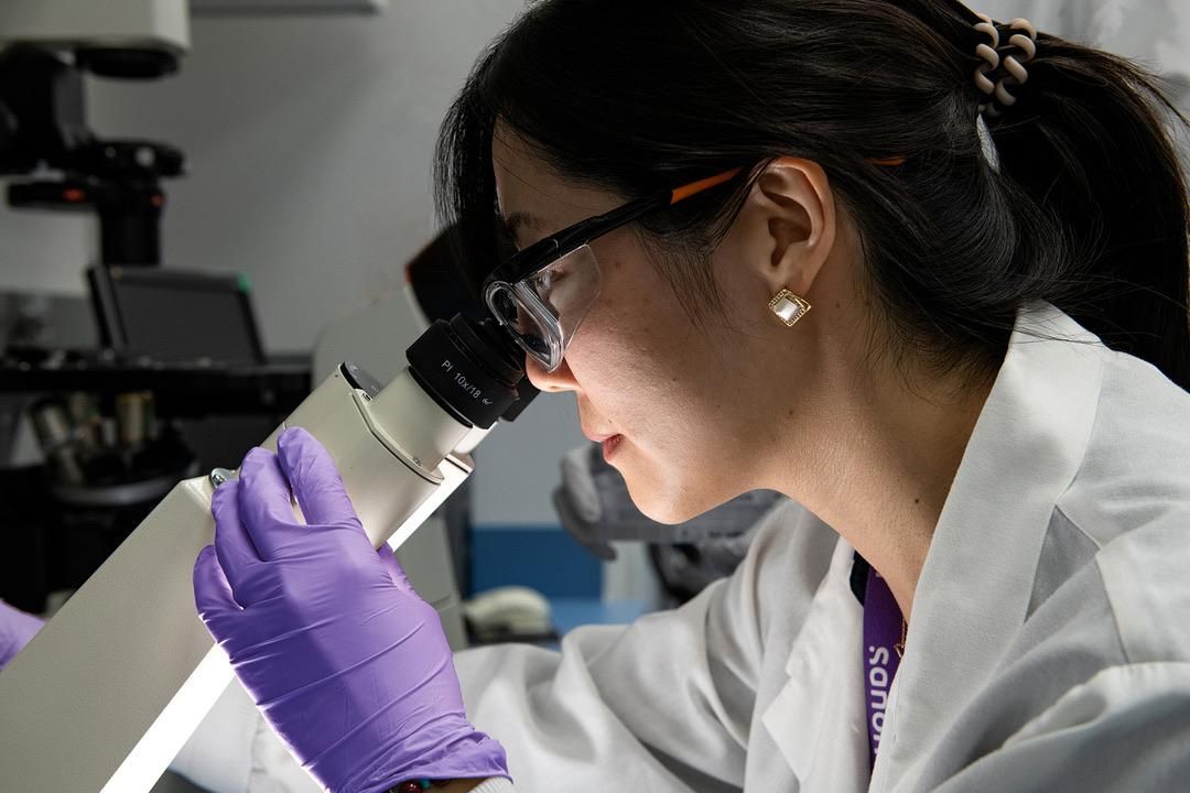 Une scientifique en blouse de laboratoire observe au microscope dans son laboratoire