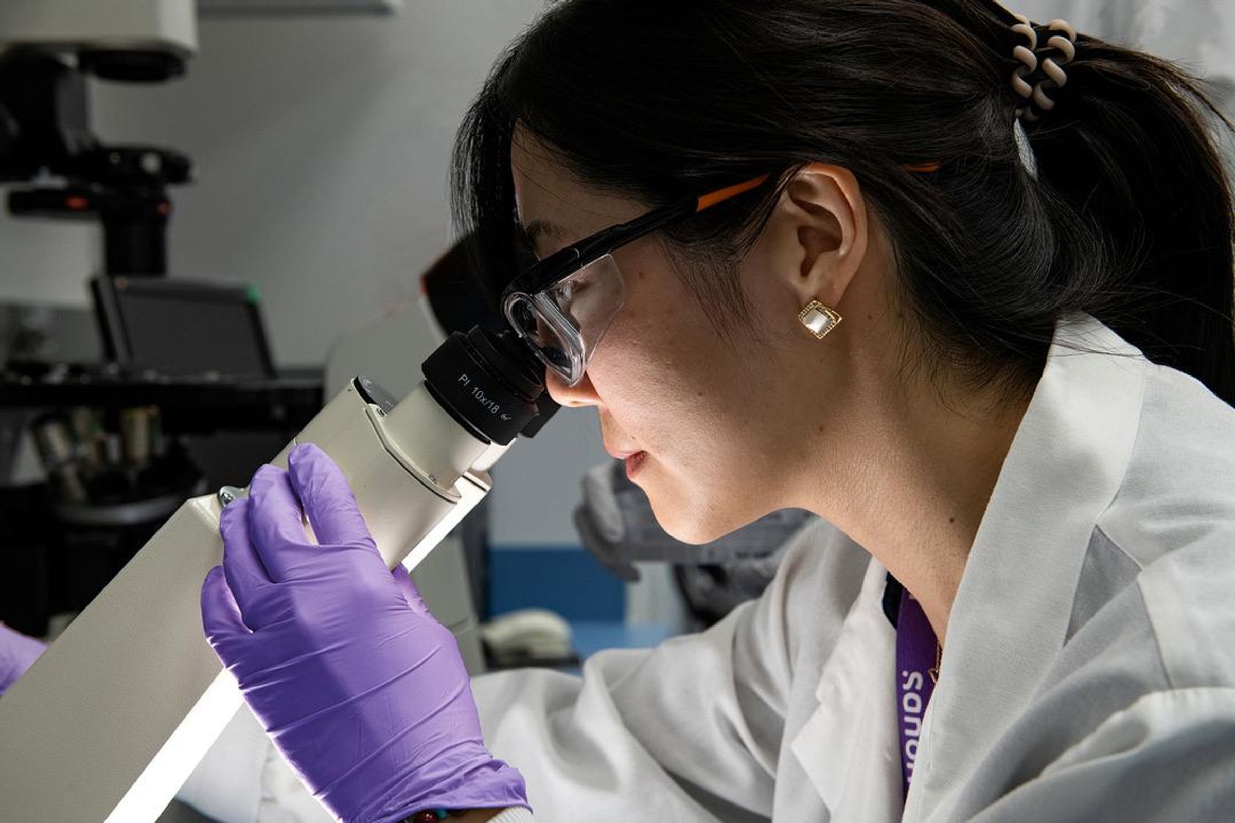 Une scientifique en blouse de laboratoire observe au microscope dans son laboratoire