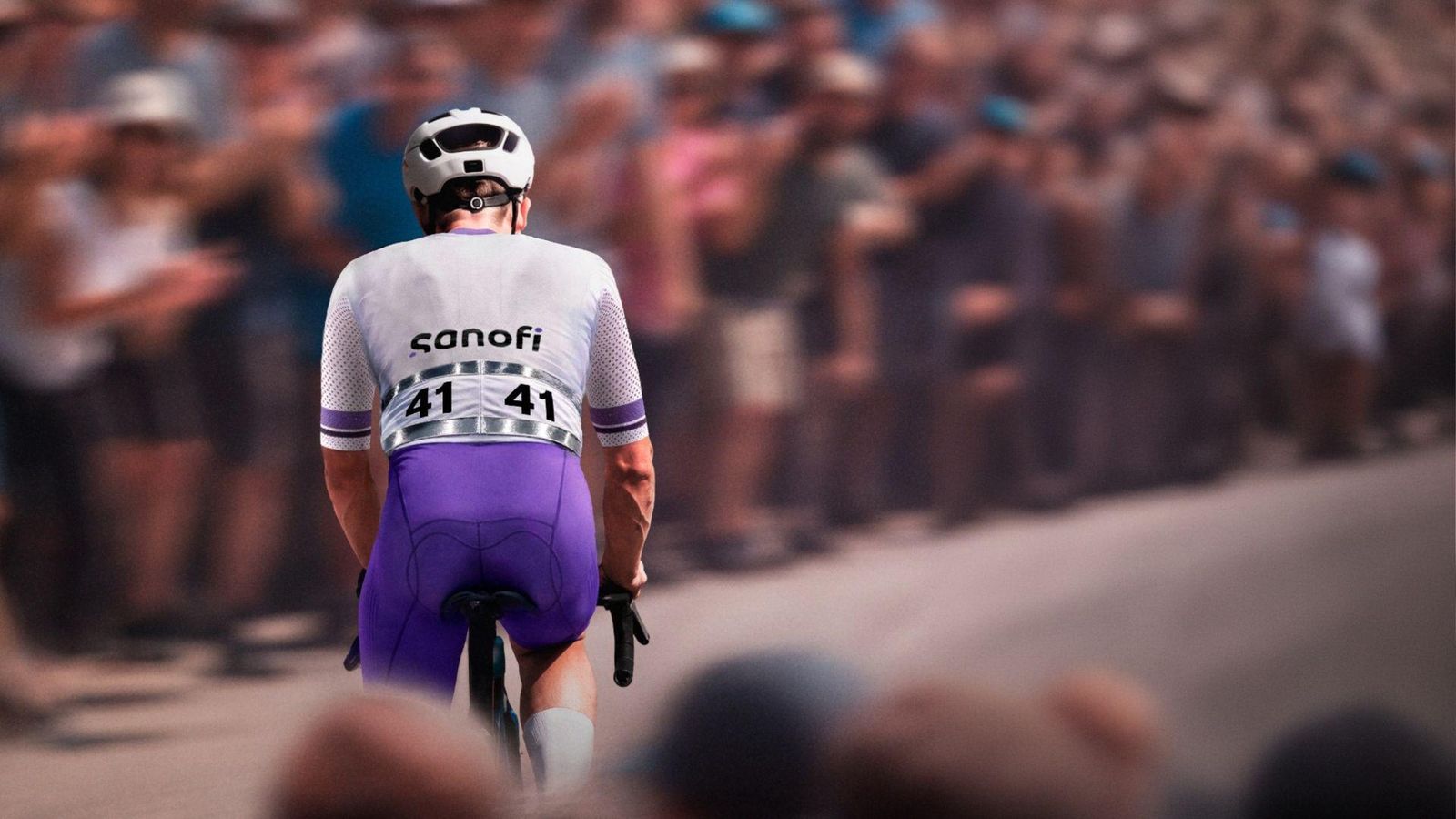Cyclist riding from behind, wearing the white jersey with purple accents, sponsored by Sanofi, with cheering spectators lining the road.