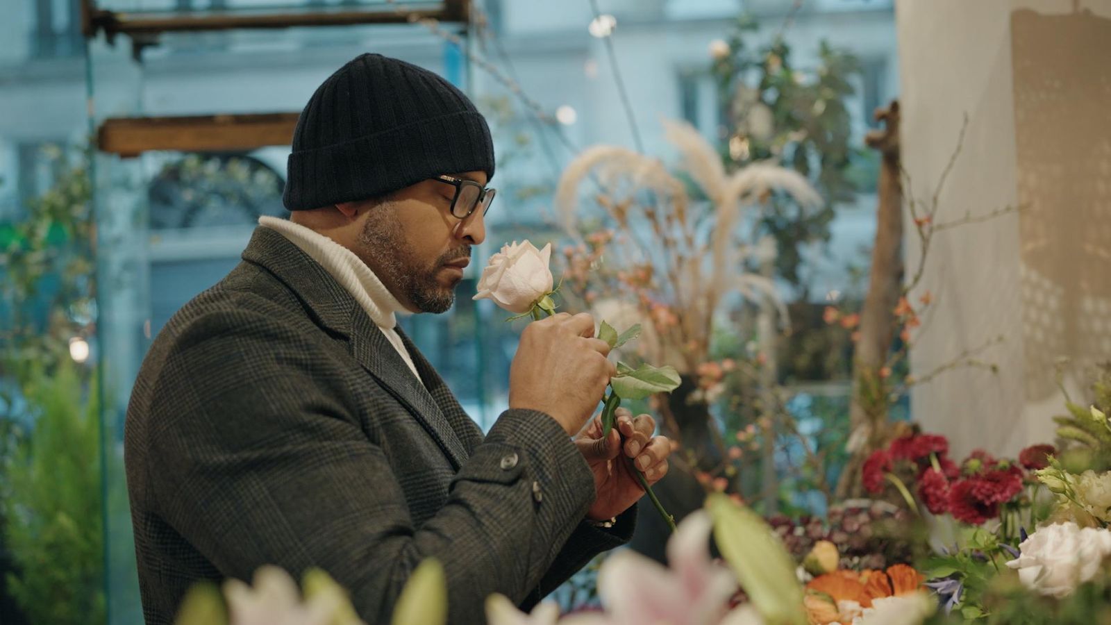 Paul Rowe, Medical Lead, US, smelling a pink rose in a flower shop, wearing glasses and a beanie