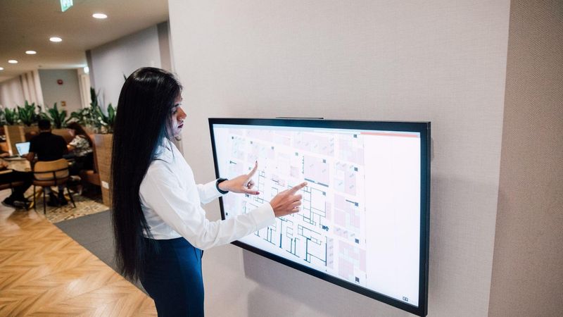 A person interacting with a large digital touchscreen displaying a visual interface in an office environment.