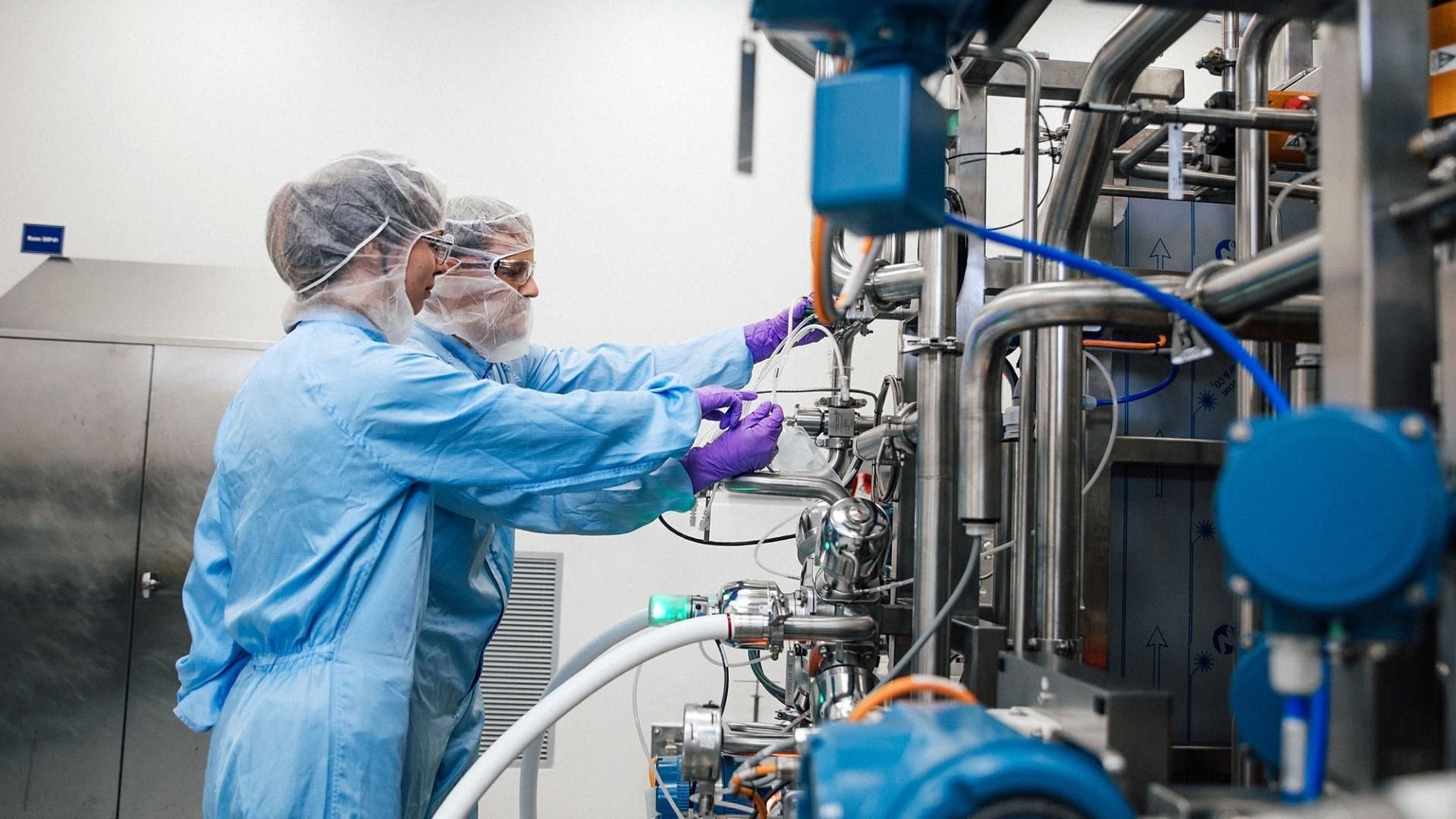 Two people in protective clothing operating industrial equipment in a manufacturing facility.