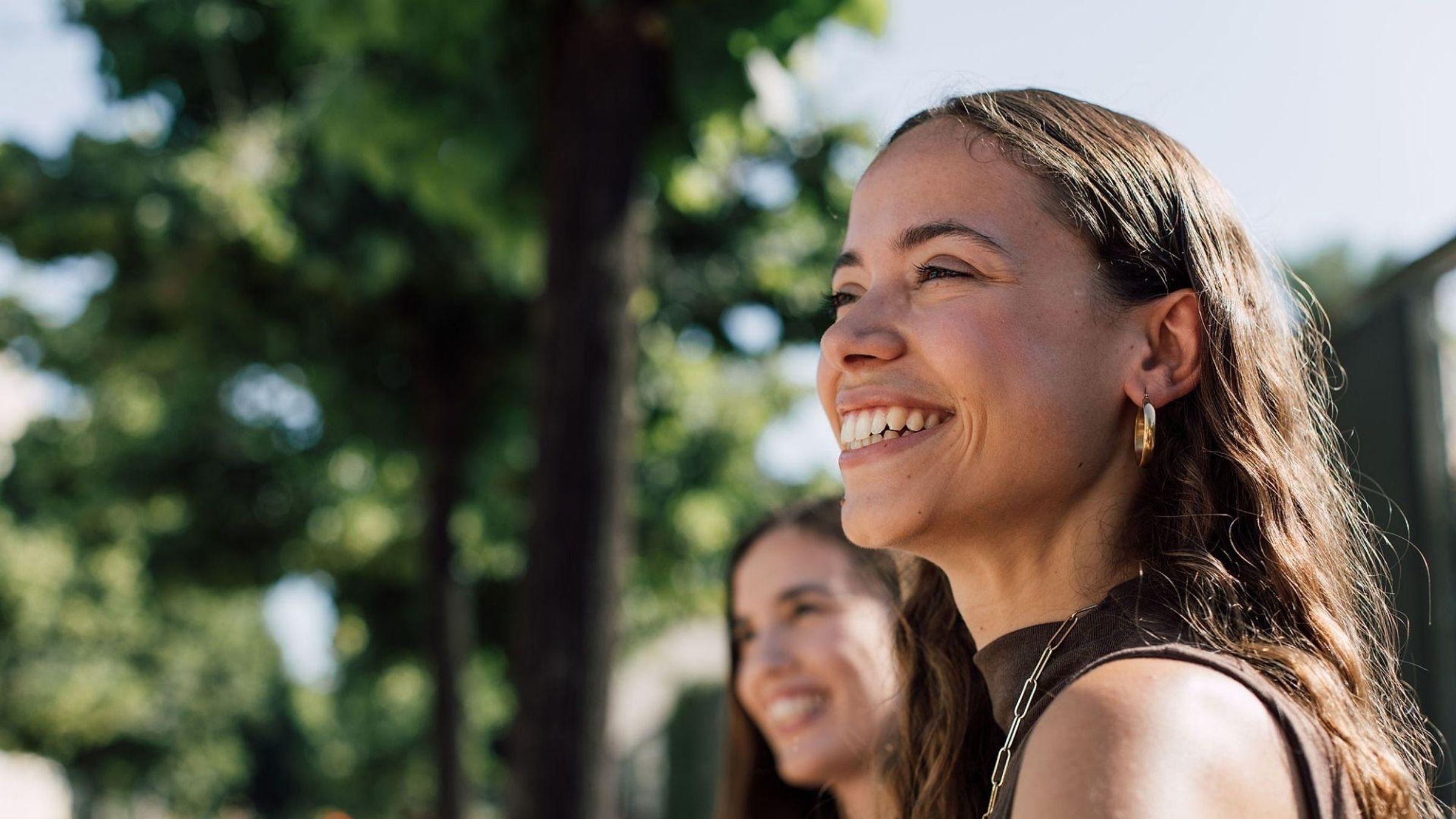 Deux femmes riant ensemble en plein air dans un parc ensoleillé avec des arbres verts en arrière-plan