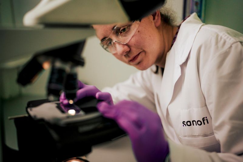 An-Sophie Claerbout is wearing a white lab coat and purple gloves, and prepares a slide in a microscope