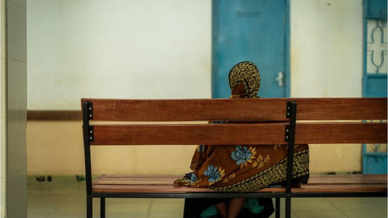 A patient facing away, sitting on a wooden bench in front of a white wall and blue door